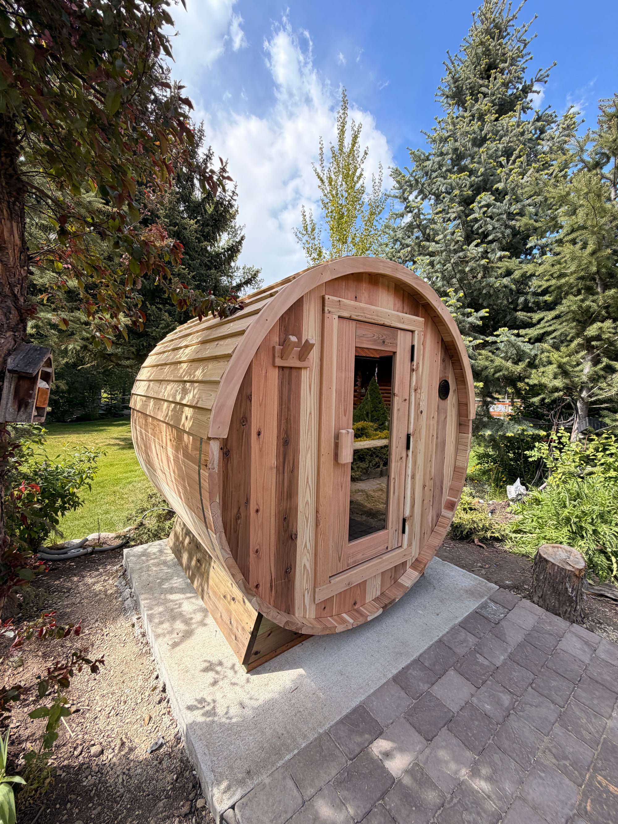 Cedar barrel sauna in a lush backyard garden